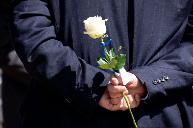Person with arms clasped behind their back holding a white rose
